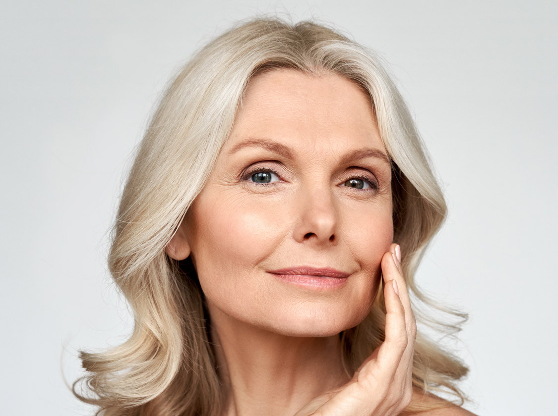 Mature woman with silver hair gently touching her cheek